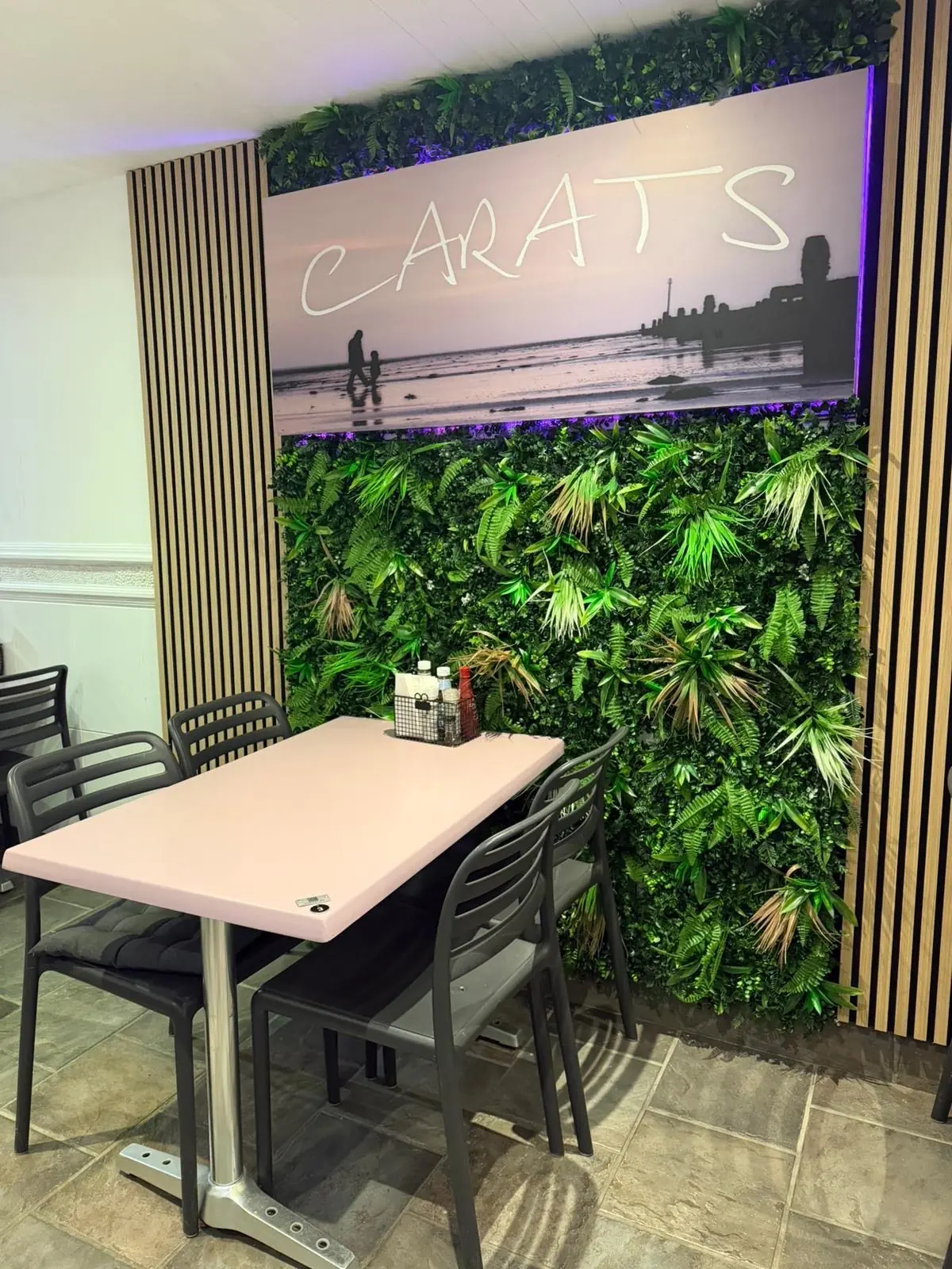 A table by the plant wall under a beach mural with the Carats name