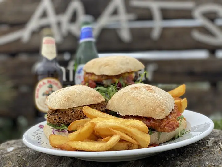 Two burgers and chips with a bottle of beer