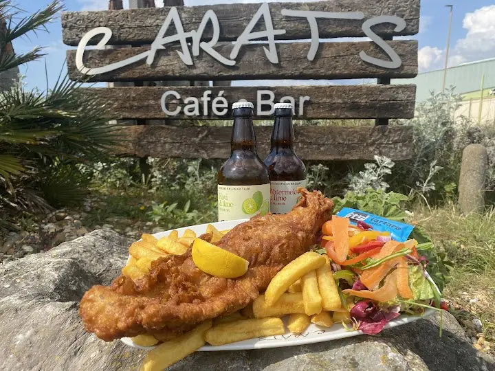 Fish and chips with lemon and salad in front of the Carats sign