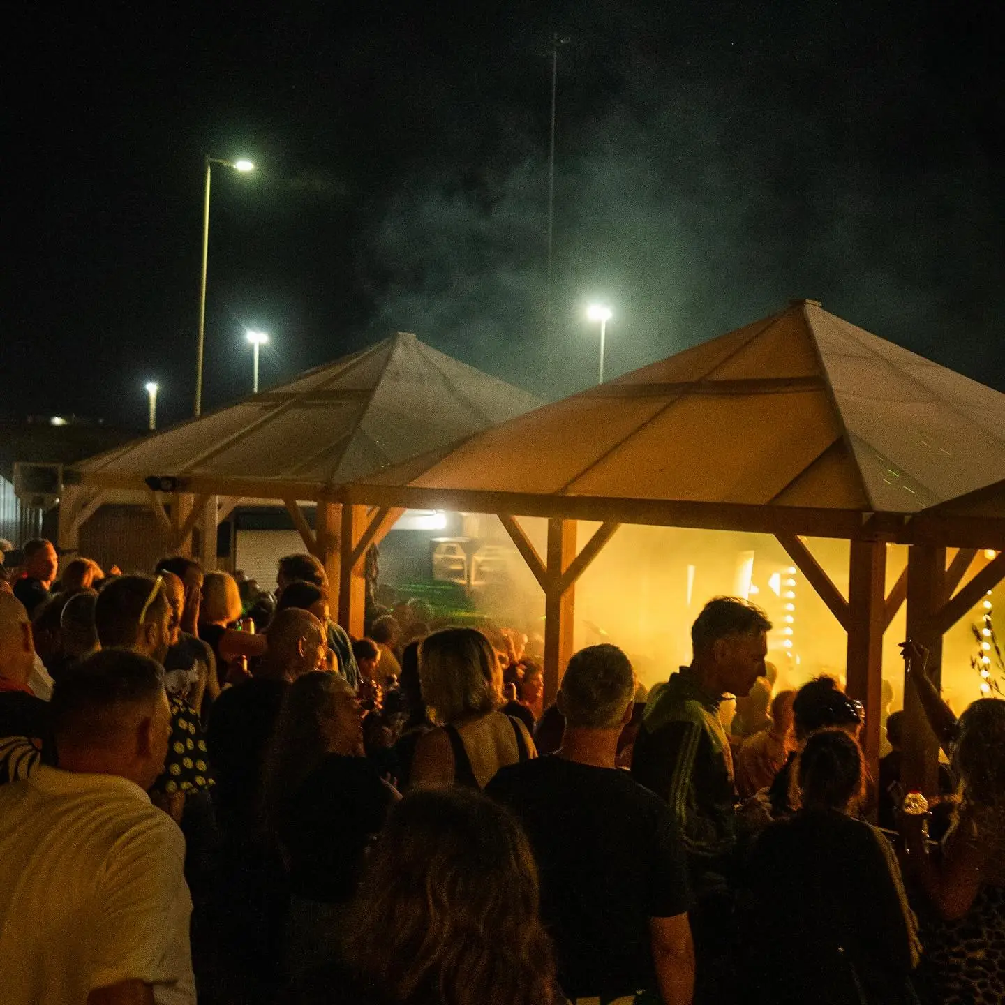A crowd under the lit canopy of the open-air stage at night