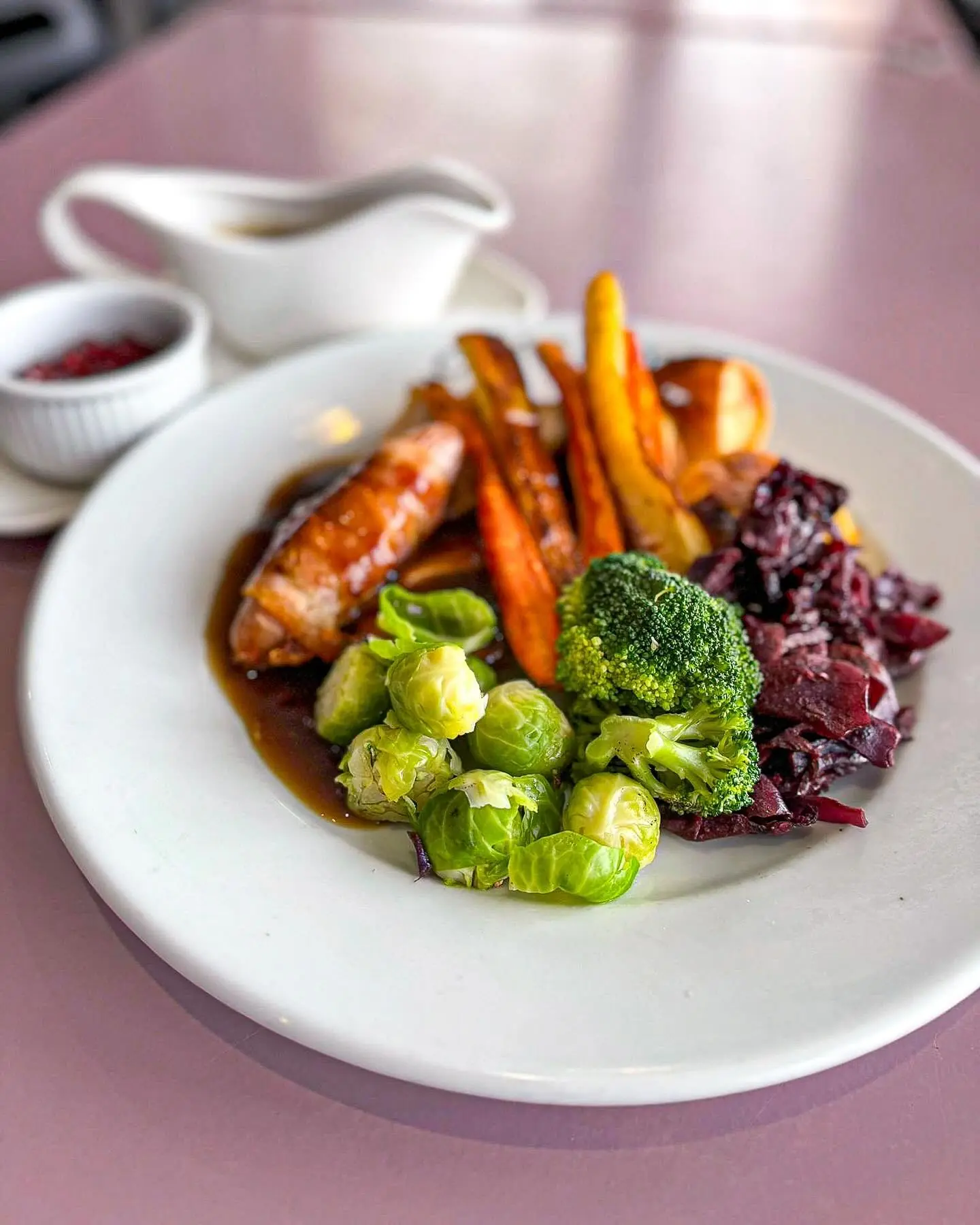 A roast dinner with sausage, roast potatoes, carrots, broccoli, sprouts and gravy